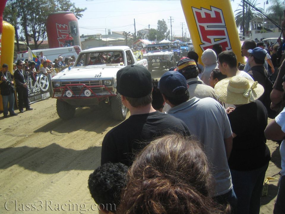 White Ford-style race truck #349 under Tecate arch in crowd