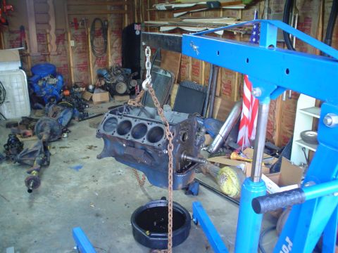 1976 Ford F-100 - An engine block is suspended by a chain hoist, ready for removal or installation in a workshop.