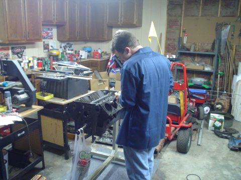 1976 Ford F-100 - Mechanic works on an engine block in a garage filled with tools and equipment.