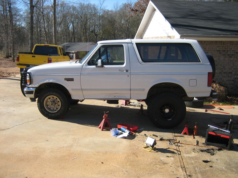 White Ford Bronco on jack stands in a driveway during a suspension lift install