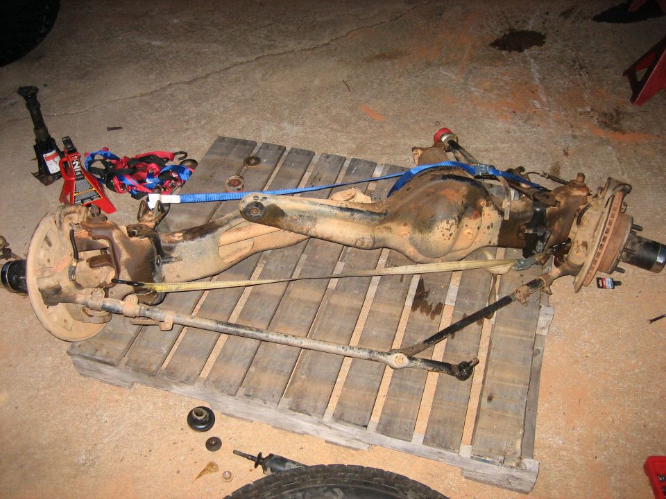 Tan-painted front solid axle assembly with rotors and tie rod resting on a wooden pallet