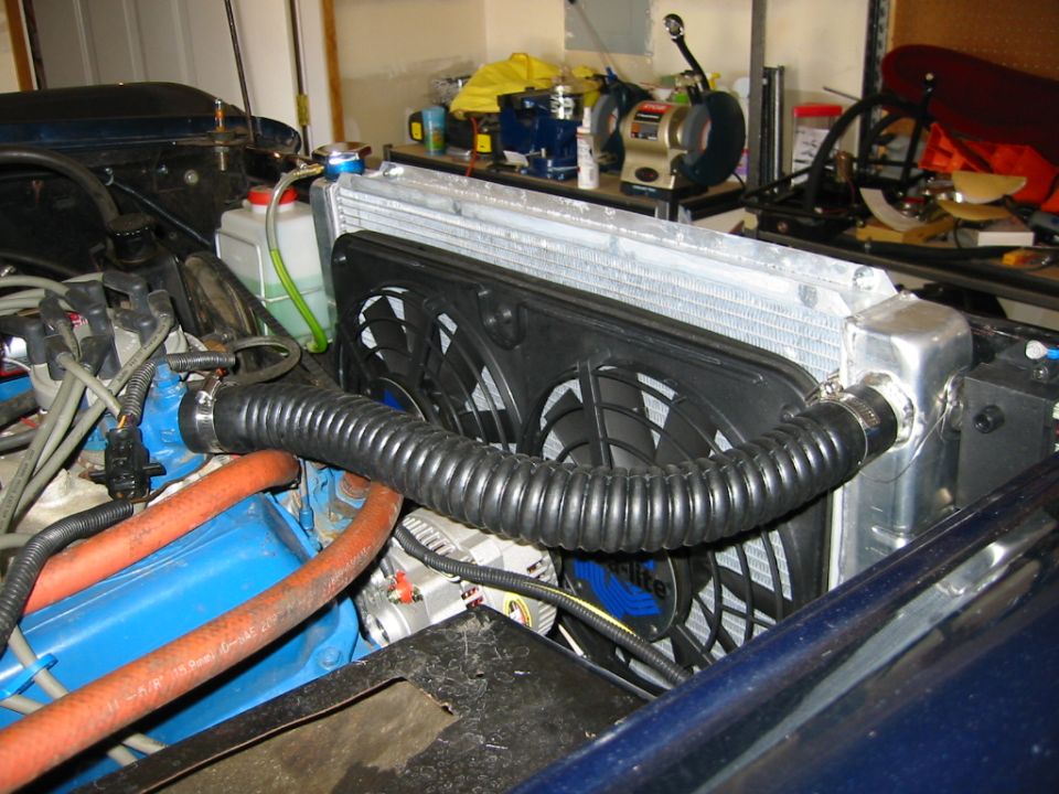 Engine bay showing a large aluminum radiator with dual electric fans, blue engine block, and orange hoses