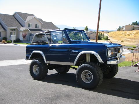 1979 Ford Bronco - Lifted blue Ford Bronco with a roll cage, parked in front of a suburban house.