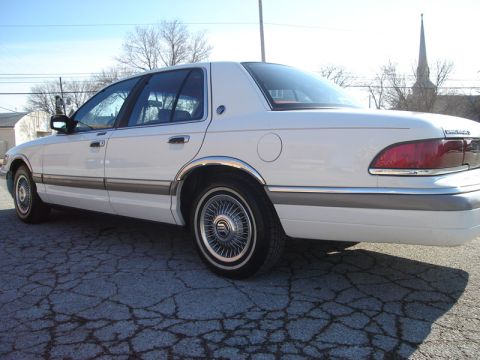 1992 Ford Crown Victoria - This white sedan has chrome trim and wire wheel covers, with a church steeple in the background.
