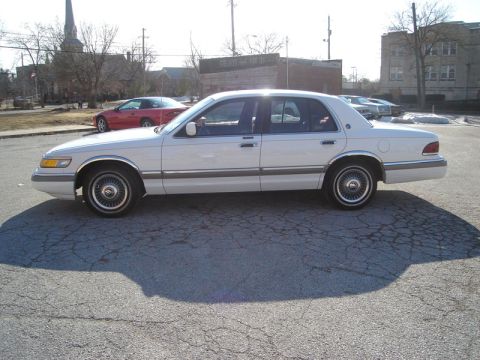 1992 Ford Crown Victoria - A white 1992 Ford Crown Victoria sedan is parked on asphalt, with a red sports car visible in the background.