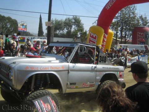 1990 Ford Bronco - Side view of a silver West Coast Broncos off-road race truck number 348 with oversized tires and sponsor decals.