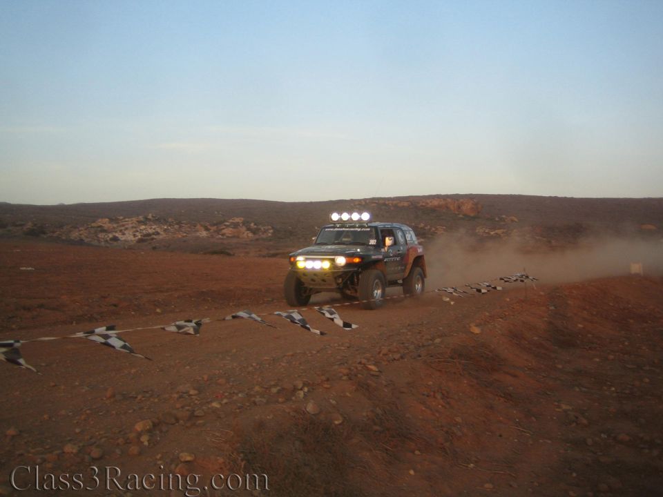 Off-road vehicle with roof light bar driving across rocky desert at dusk