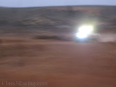 1990 Ford Bronco - blurry motion shot of bright vehicle headlights glowing in the distance across a dim reddish desert landscape.