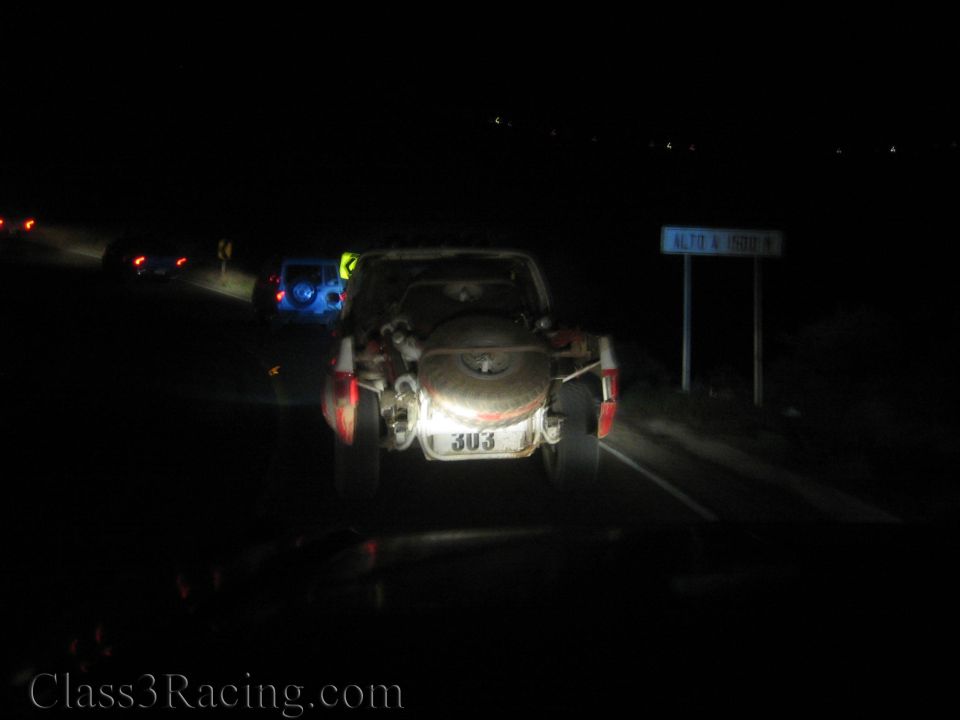 Rear of race vehicle 303 with spare tire on a dark highway by a road sign