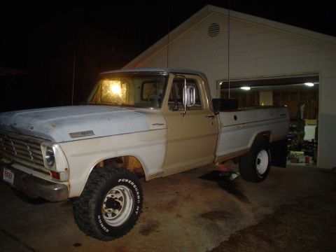 1967 Ford F-250 - A two-tone Ford F-250 pickup truck is parked outside a garage with its interior light on.