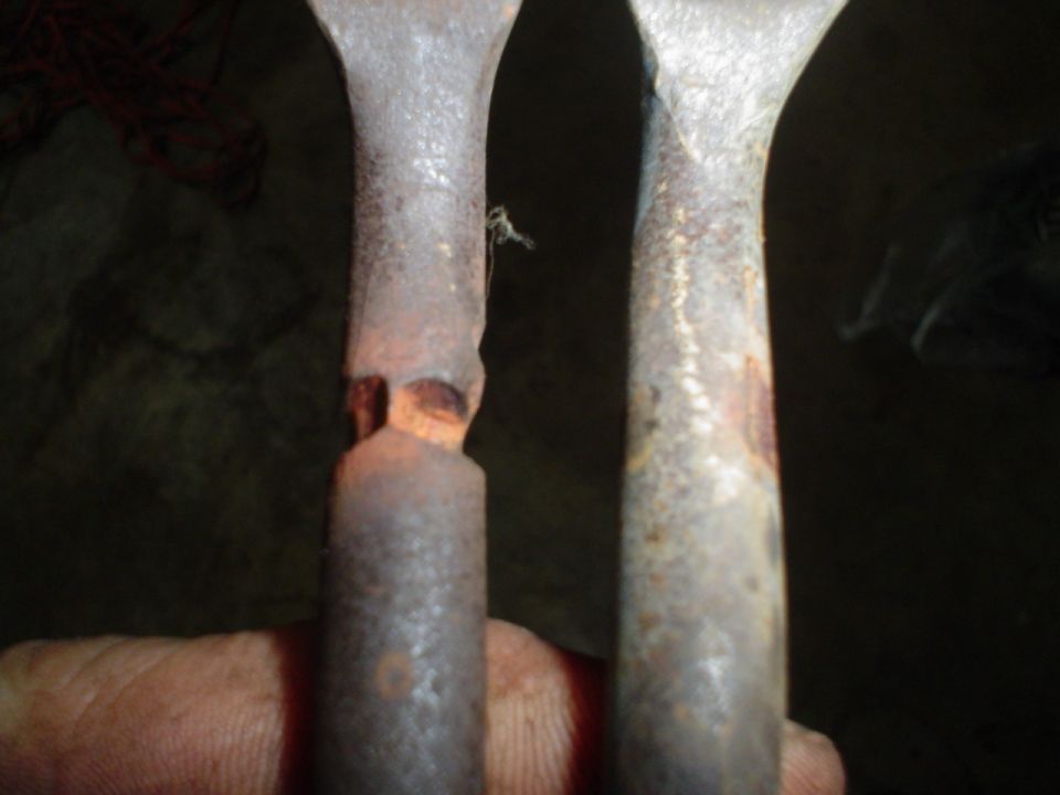 Two rusty metal rods, one with a damaged end, held by a hand