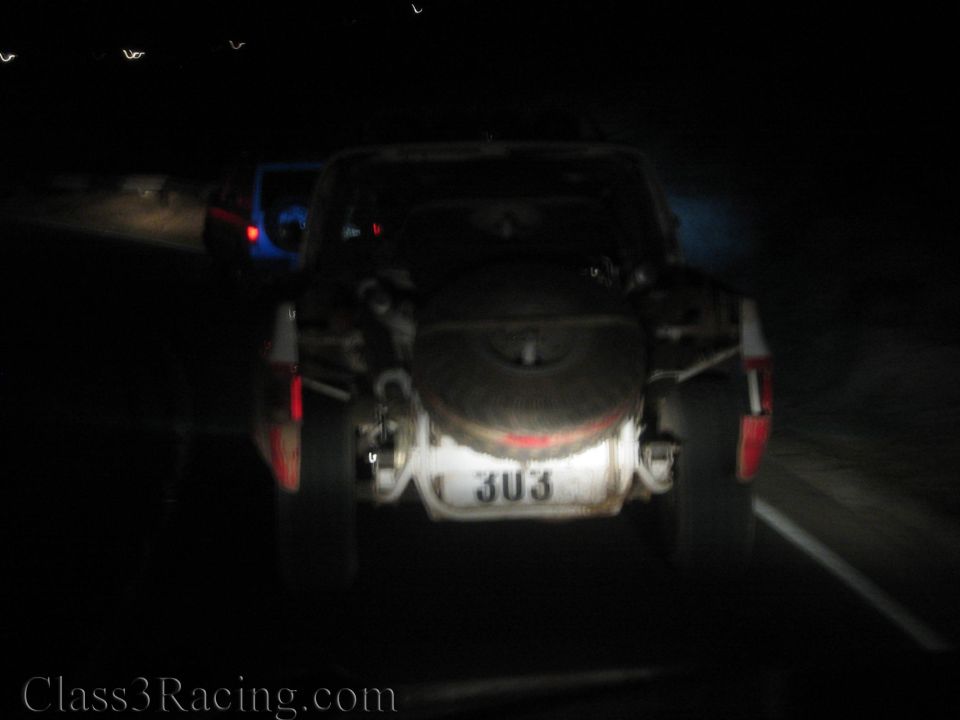 Blurry rear view of off-road truck with spare tire and plate 303 at night