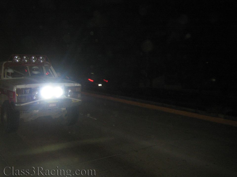 White race truck with roof lights and bright headlights on dark roadside