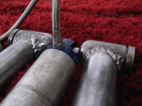 1989 Ford Bronco - Close-up of exhaust manifold pipes, showing welds and a braided hose connection.