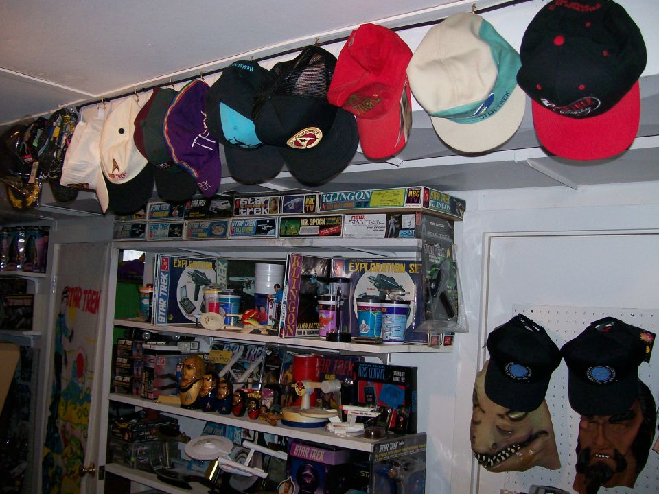 Shelves packed with Star Trek models, toys, and boxes, plus hats hanging overhead