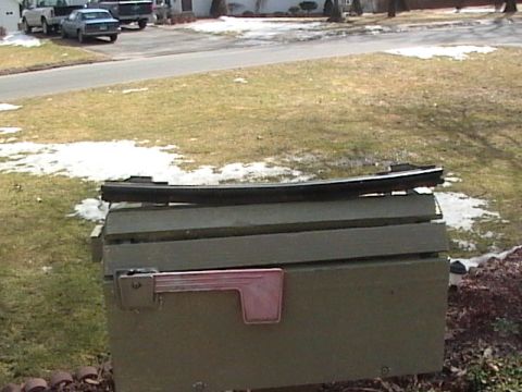 1990 Ford Bronco - A black trim piece rests on top of a green mailbox, with vehicles visible in the background.