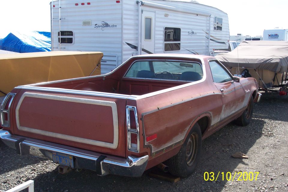 Faded red Ford Ranchero in a storage yard, rear three-quarter view showing tailgate trim frame