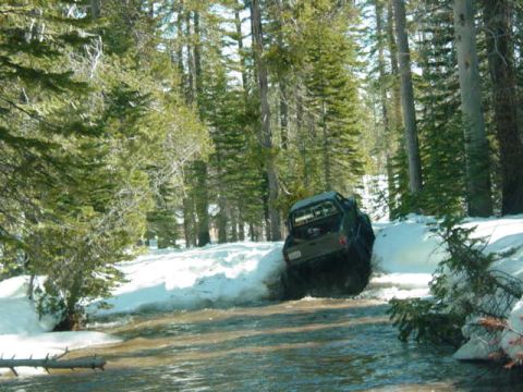 1986 Ford Bronco - Vehicle navigates a snowy, watery trail in a forest setting.