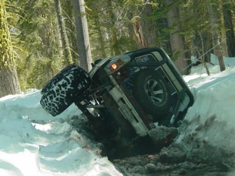 1986 Ford Bronco - An off-road vehicle is stuck in a snow-covered ditch, tilted precariously on its side.
