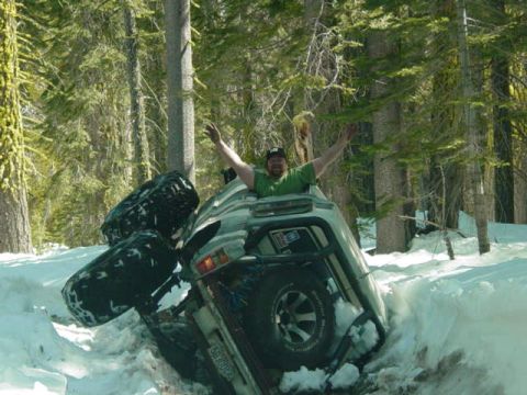 1986 Ford Bronco - A person celebrates while their off-road vehicle is stuck deep in a snowbank in a wooded area.