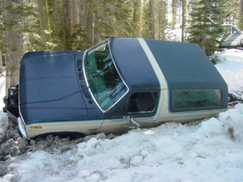 1986 Ford Bronco - A blue and tan Ford Bronco is partially buried in snow, with another vehicle visible in the background.