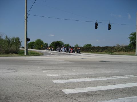 1986 Ford Bronco - A group of motorcycles waits at a traffic light at an intersection on a sunny day.