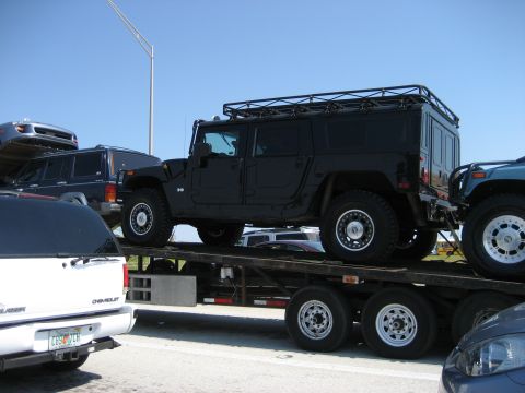 1986 Ford Bronco - A black Hummer H1 wagon is transported on a trailer alongside other vehicles under a clear blue sky.
