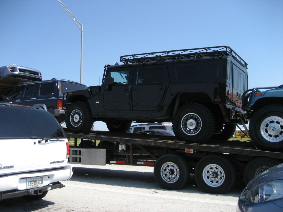 Black Hummer H1 wagon on a car carrier trailer, with other vehicles visible