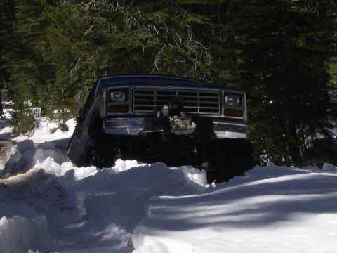 1986 Ford Bronco - A dark 1980s Ford Bronco navigates through deep snow, its front winch visible.