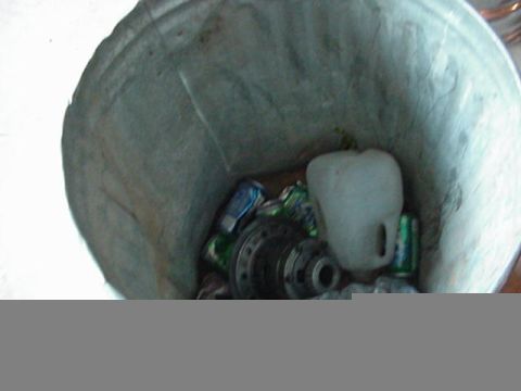 1992 Ford Bronco - Looking down into a galvanized metal trash can holding discarded parts, a cast-iron hub or brake drum/axle flange assembly and a white plas…