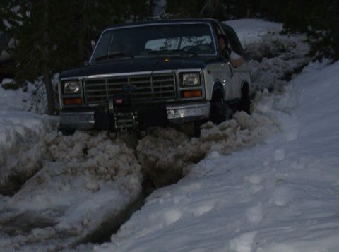 1986 Ford Bronco - A Ford Bronco navigates through deep snow, its front end partially submerged.