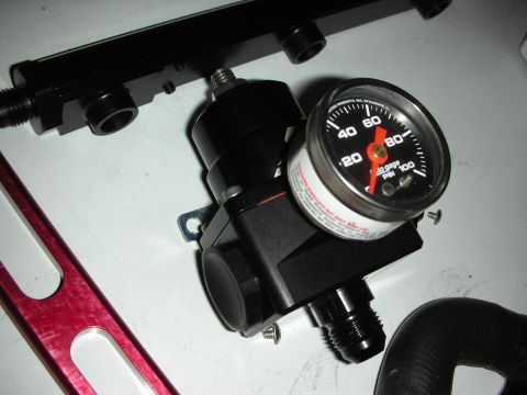 1992 Ford Crown Victoria - A black fuel pressure regulator and gauge are shown next to a black fuel rail and a red bracket.