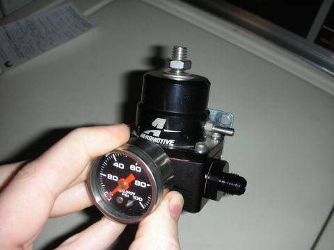 1992 Ford Crown Victoria - A hand holds a fuel pressure regulator with an Aeromotive logo and a gauge displaying 20 PSI.