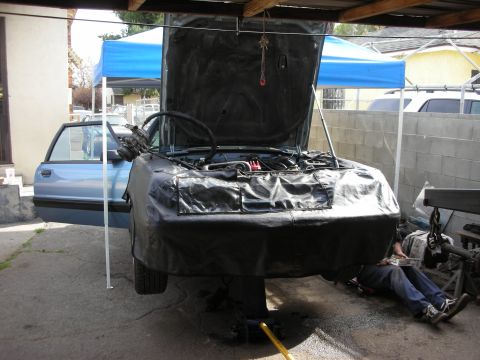 1990 Ford Mustang - Car on a lift with hood open, undergoing engine work. A person is visible underneath.