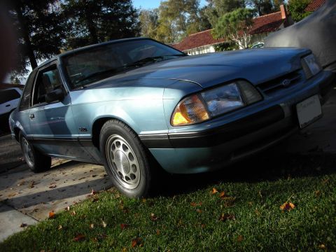 1990 Ford Mustang - A blue 1990 Ford Mustang is parked on a lawn with fallen leaves.