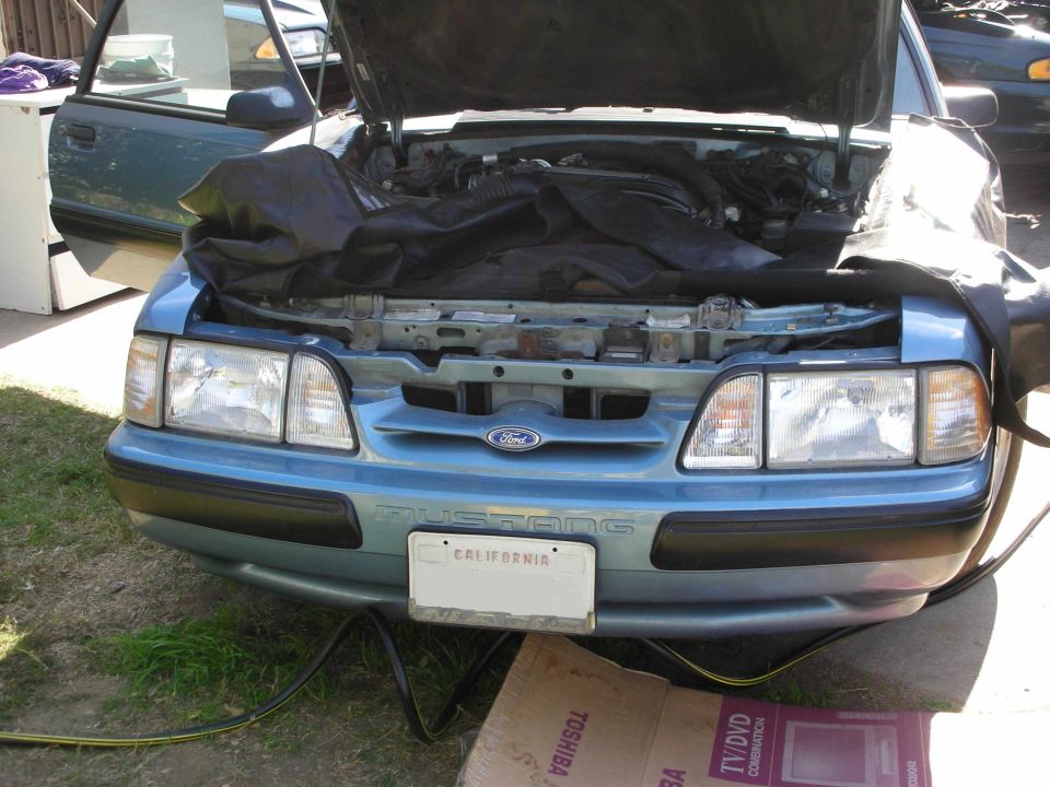 Blue 1990 Ford Mustang front view with hood open, showing engine covered by a black tarp