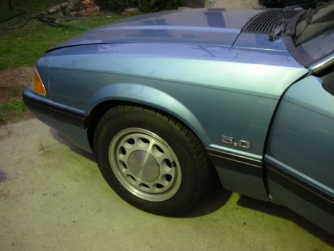 1990 Ford Mustang - Close-up of a blue 1990 Ford Mustang's front fender and wheel, showing the 5.0 badge.