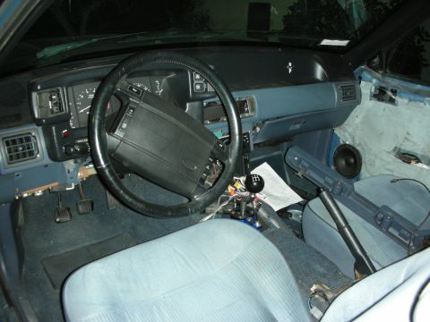 1990 Ford Mustang - The interior of a 1990 Ford Mustang shows light blue upholstery and a black steering wheel with visible wear and tear.
