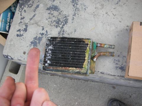 1990 Ford Mustang - A used heater core is shown resting on a concrete ledge, with a box and a partial water pump box in the background.