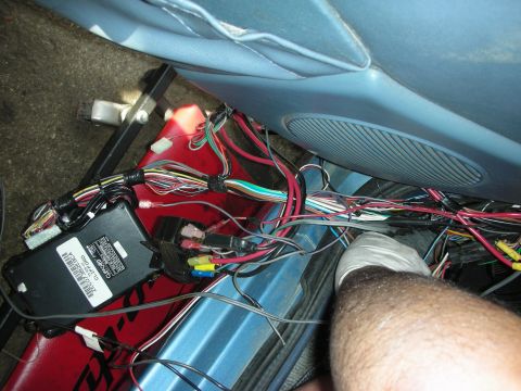 1990 Ford Mustang - Close-up of a car's interior wiring harness, a Clifford alarm module and fuse box, with a gloved hand visible.