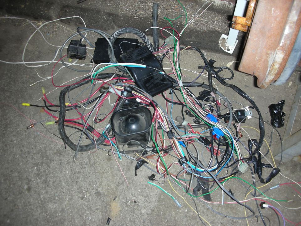 Tangled automotive wiring harness with black plastic connectors and various colored wires on a concrete floor