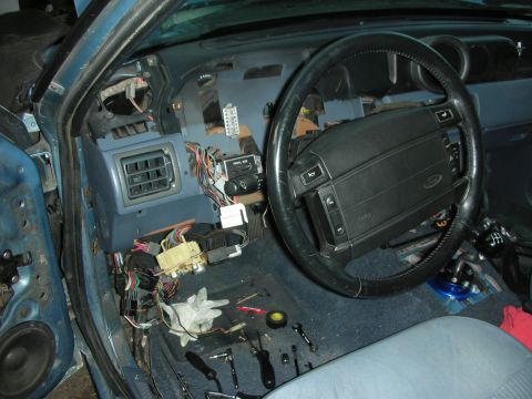 1990 Ford Mustang - The dashboard of a 1990 Ford Mustang is partially disassembled, revealing wiring and tools on the floor.