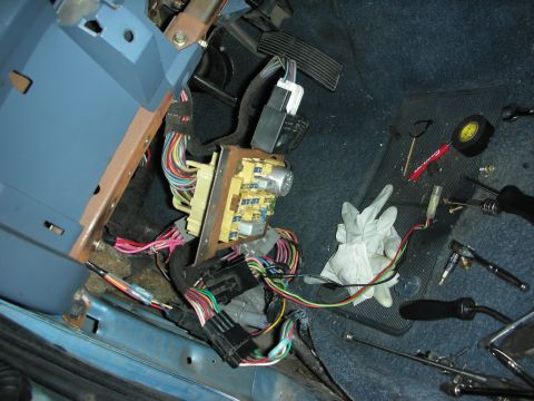 1990 Ford Mustang - The interior of a 1990 Ford Mustang reveals a complex wiring harness and fuse box, with tools scattered on the blue carpet.