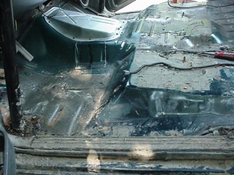 1992 Ford Bronco - The bare interior floor pan of a vehicle with the carpet removed, showing the green-painted transmission tunnel, seat mounting holes, wirin…