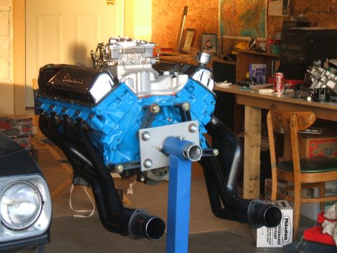 1974 Ford Ranchero - A blue V8 engine with black exhaust headers is mounted on a stand in a workshop.