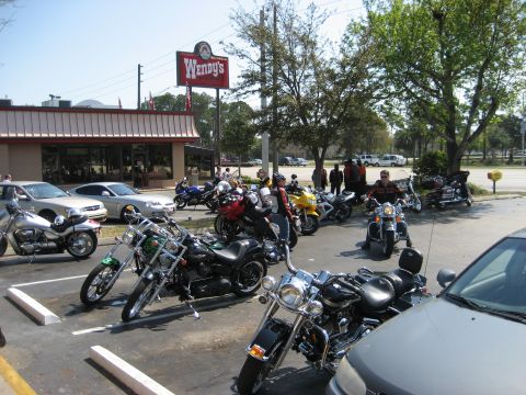 1986 Ford Bronco - A group of motorcycles and cars are parked in a lot outside a Wendy's restaurant on a sunny day.