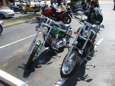 1986 Ford Bronco - Two custom choppers, one green with flames and one black, are parked in a lot on a sunny day.