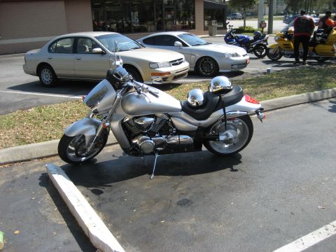 1986 Ford Bronco - A silver cruiser motorcycle is parked in a lot with other vehicles visible in the background.