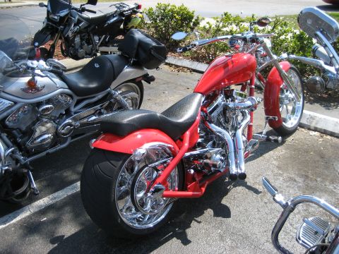 1986 Ford Bronco - Multiple motorcycles are parked in a lot, including a bright red custom bike with extensive chrome detailing.