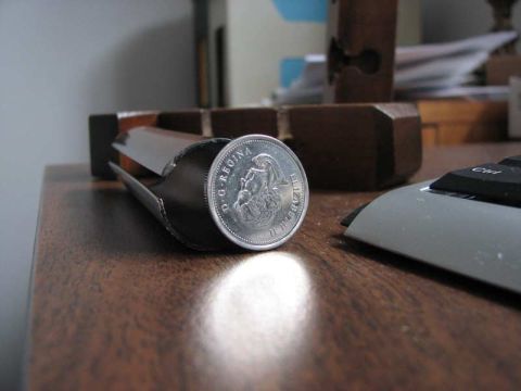 2003 Ford Crown Victoria - A coin is placed inside a stapler, resting on a wooden desk surface.